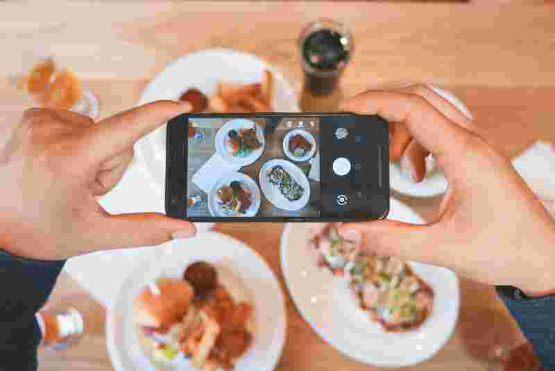 Gehaltenes Handy, mit dem gerade ein ausgiebiges schönes Frühstück fotografiert wird - Ratgeber Social Media Studium: Campus M University.