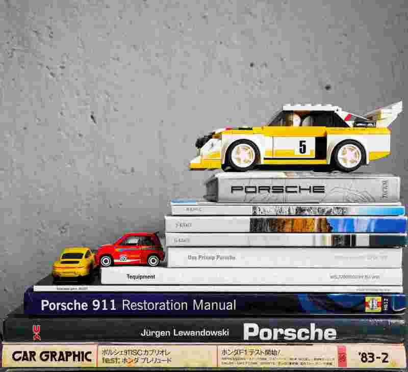 Kleine Modellautos auf einem Stapel Bücher über Porsche auf einem Tisch - Symbolbild für das Automobilbusiness.
