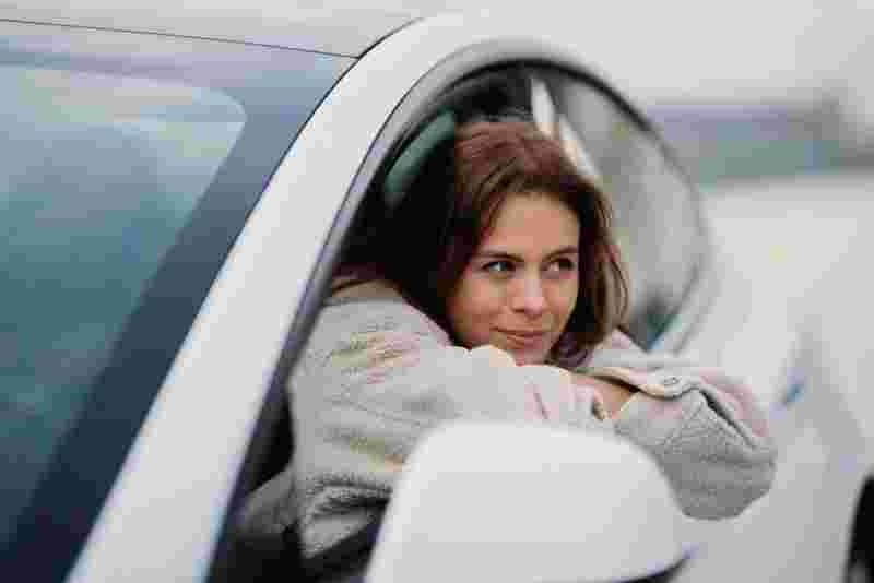 Frau im grauen Mantel lehnt aus einem weißen Auto – Informationen zum staatlich anerkannten Automobilwirtschaft Studium.