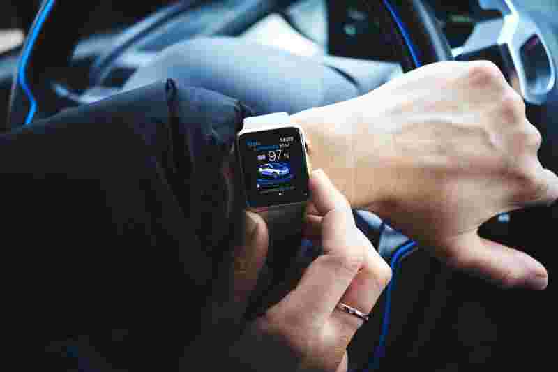 Eine Hand mit einer Apple Watch, auf der eine Auto-App angezeigt wird, während jemand im Auto sitzt.