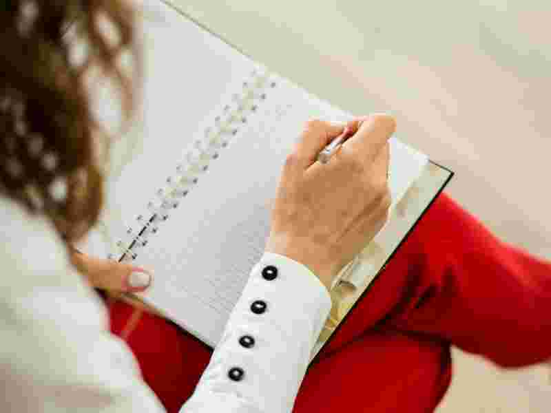Eine Frau mit roter Hose schreibt in ein Notizheft - Ratgeber Psychologie Studium: Campus M University.