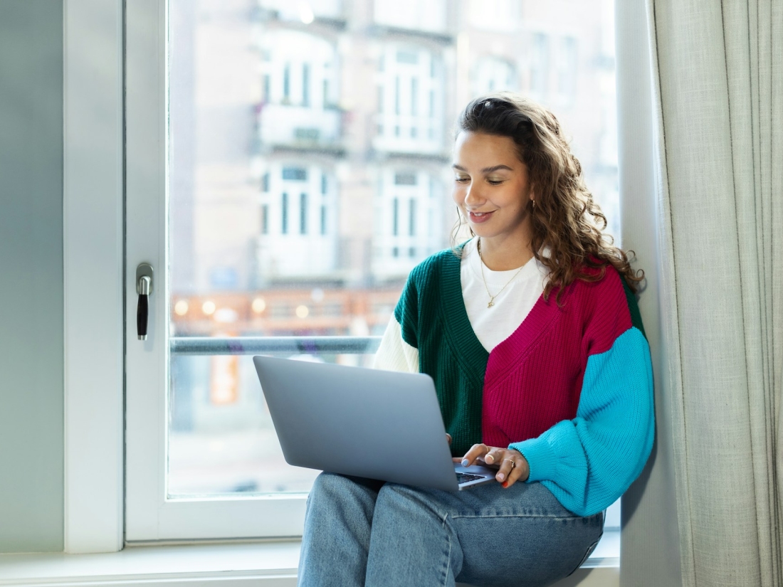 Studentin arbeitet mit einem Laptop am Fenster in urbaner Umgebung