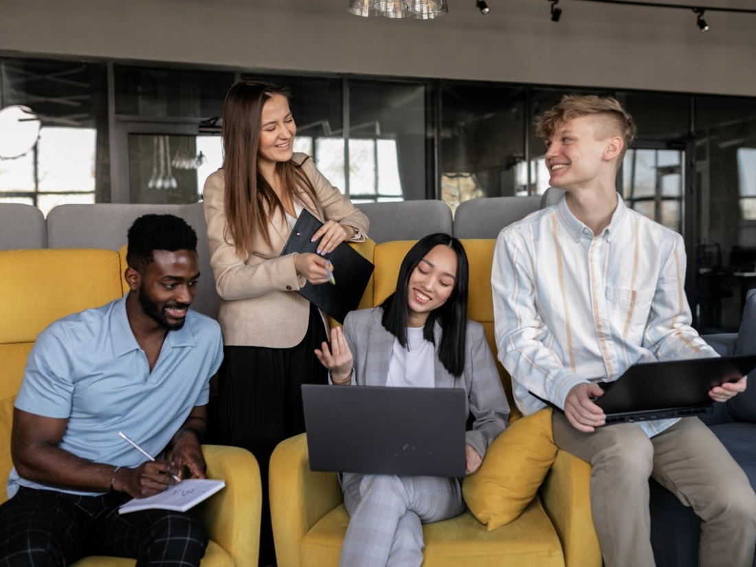 Vier Studierende arbeiten zusammen in moderner Lernumgebung mit Laptops und Notizbuch