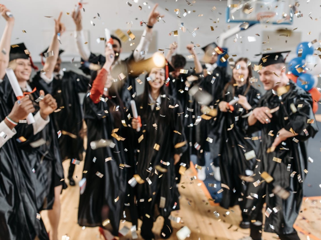 Gruppe von Absolvierenden feiert ihren Abschluss mit Urkunden und Konfett i in der Luft 13
