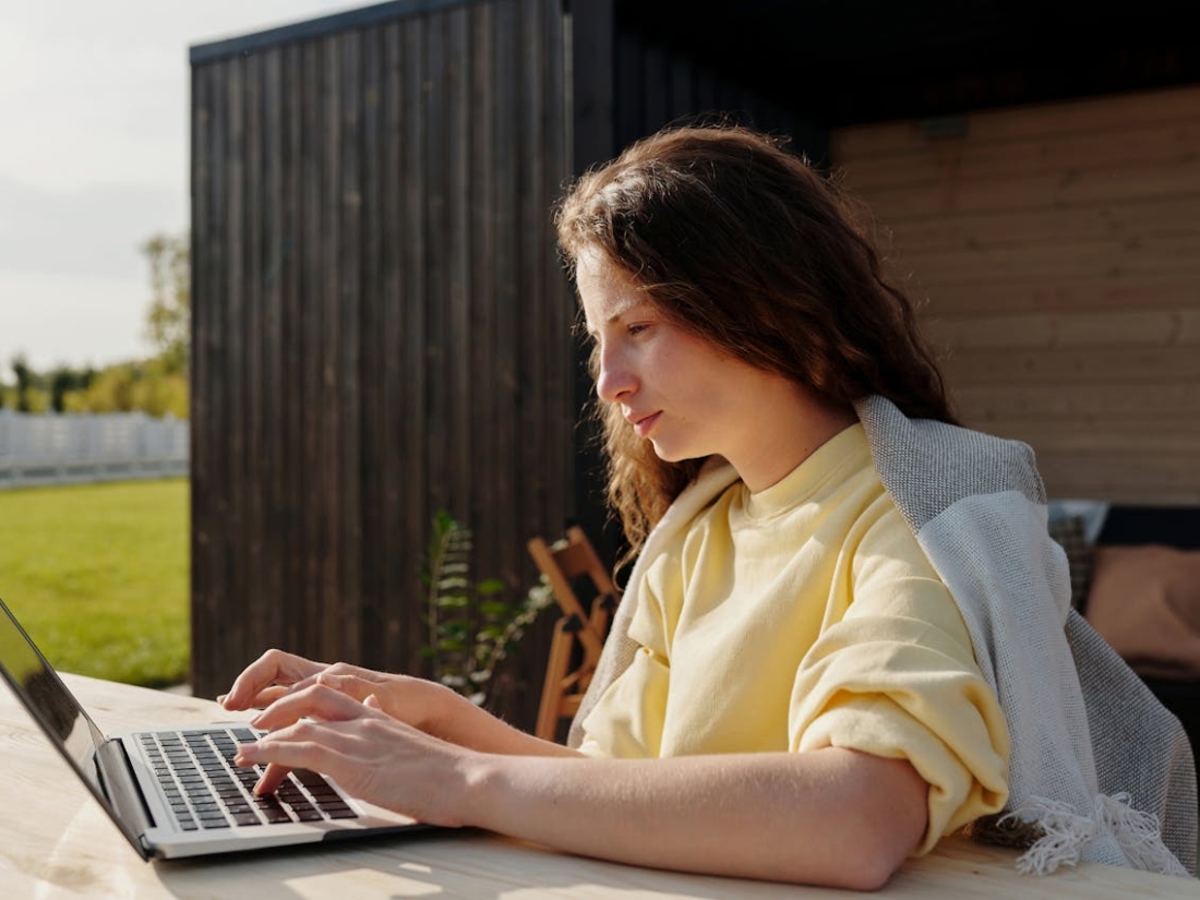 Studentin arbeitet mit Laptop an einem Tisch im Außenbereich