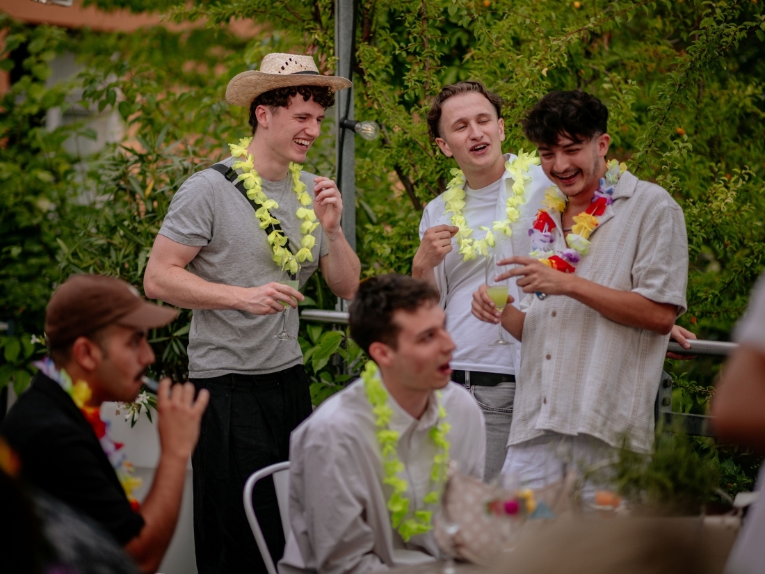 Mehrere Studierende mit Blumenkett en stehen im Freien zusammen und unterhalten sich