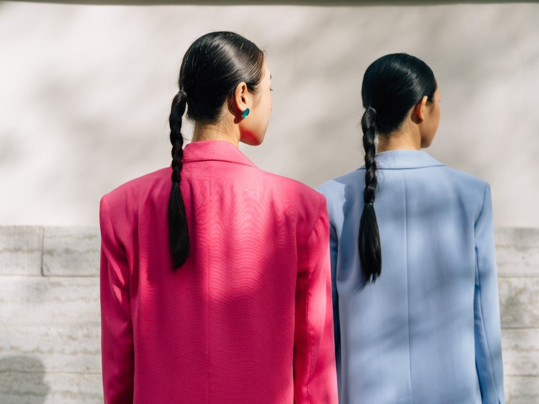 Zwei Personen stehen mit dem Rücken zur Kamera und tragen farbige Blazer in Pink und Hellblau.