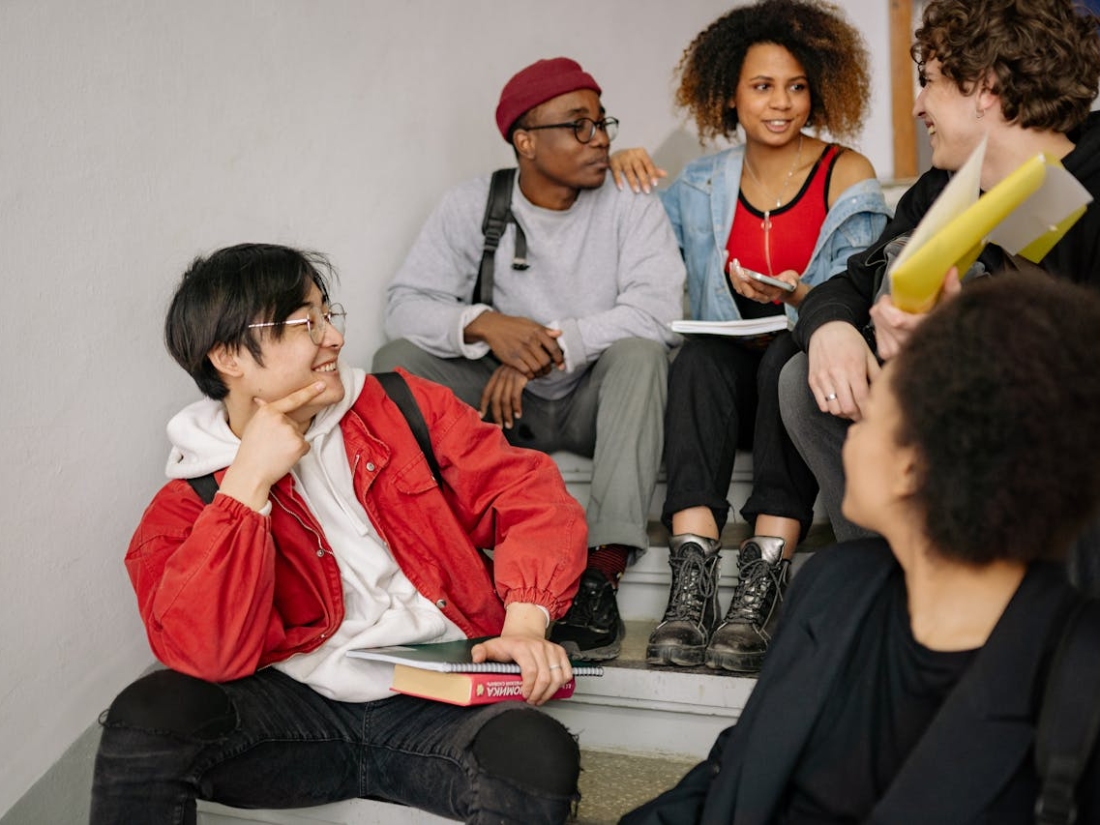 Gruppe junger Menschen sitzt auf Stufen und unterhält sich, einige halten Hefte oder Ordner.