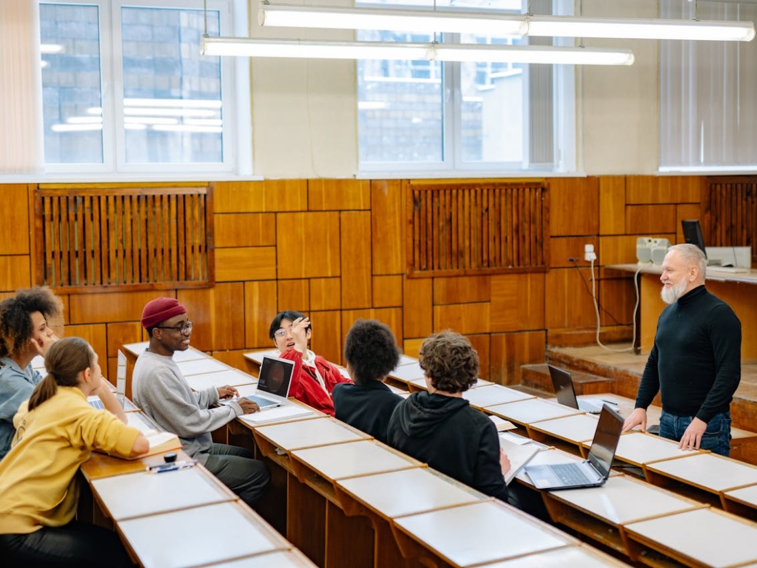 Dozent steht vor einer kleinen Gruppe Studierender in einem modernen Seminarraum.