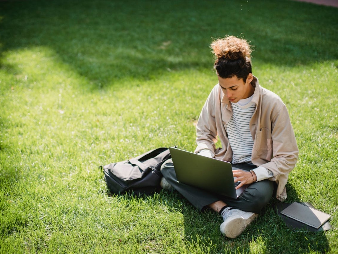 Student sitzt in der Wiese mit einem Laptop in der Hand.
