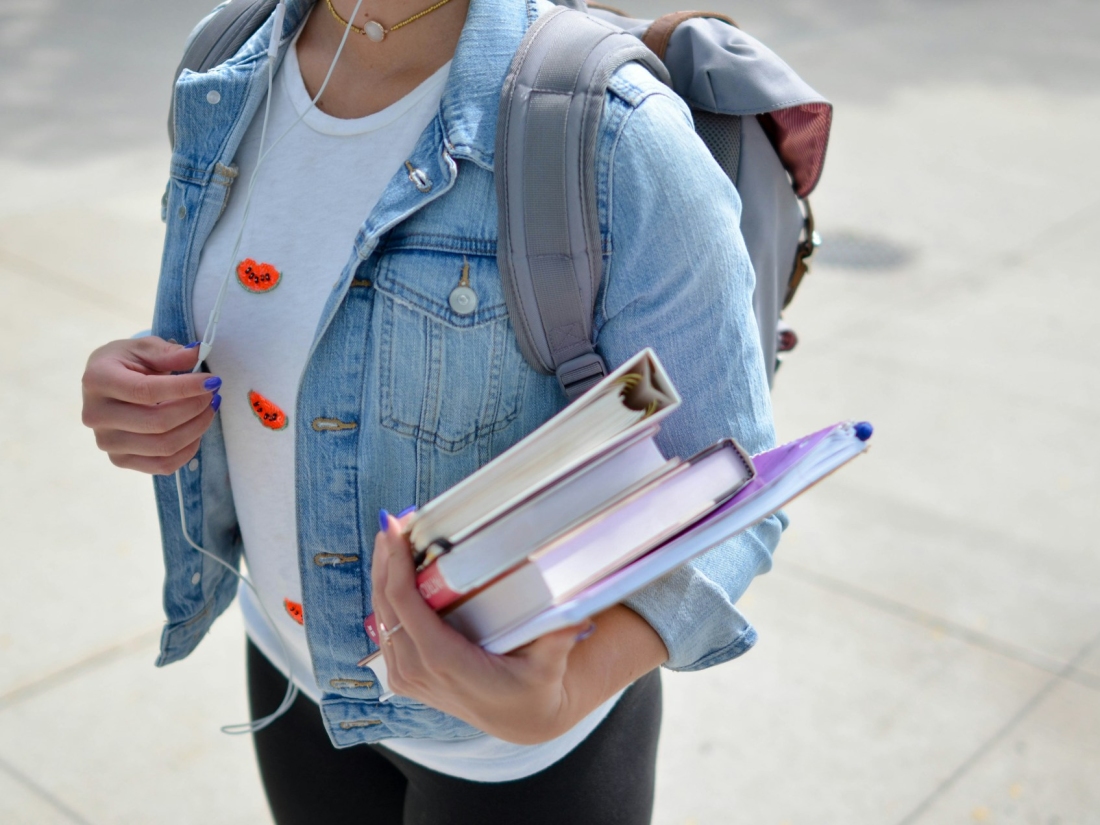 Studentin mit Büchern im Arm und Rucksack auf dem Weg zur Vorlesung – Master Sportmanagement