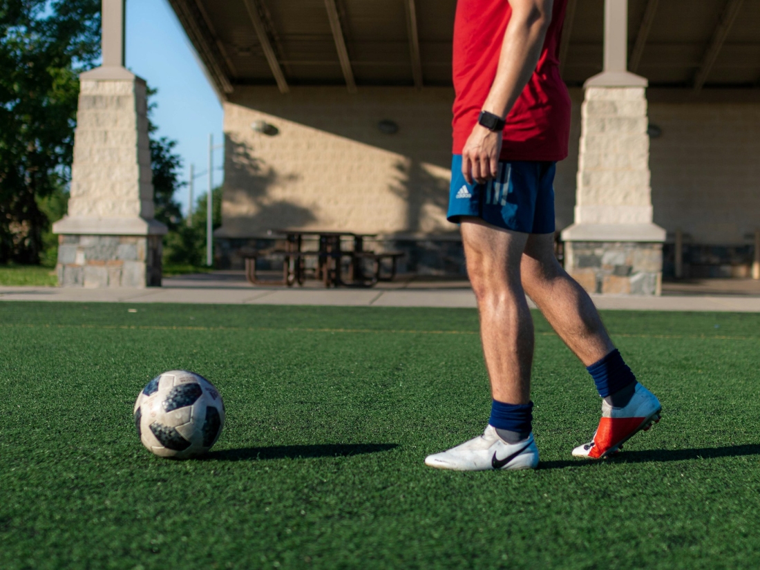 Person in rotem Hemd und blauen Shorts beim Fußballspielen – Master Sportmanagement