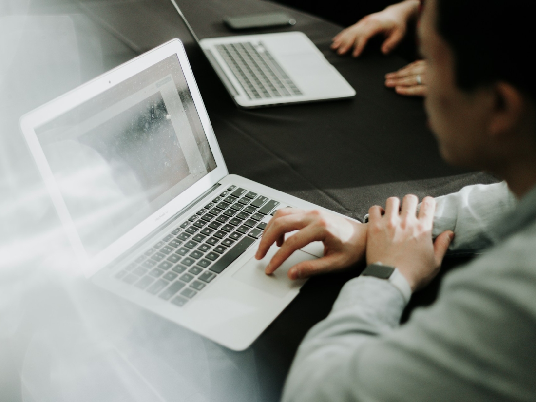 Person arbeitet an einem Laptop in einem Besprechungsraum, weitere Laptops im Hintergrund.