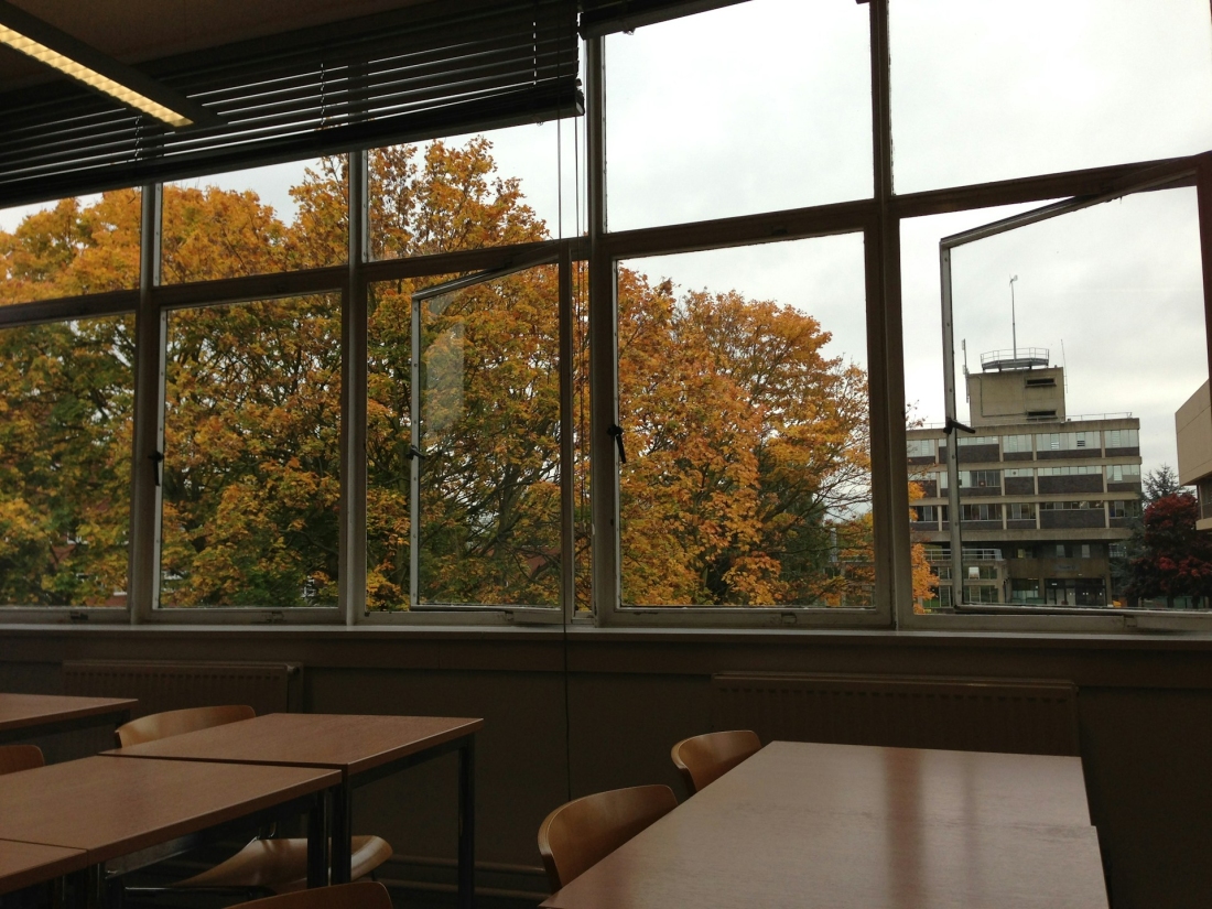 Klassenzimmer mit Blick durch geöff nete Fenster auf herbstliche Bäume