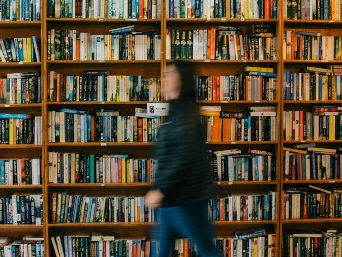 Person geht unscharf an einem Regal mit vielen Büchern vorbei